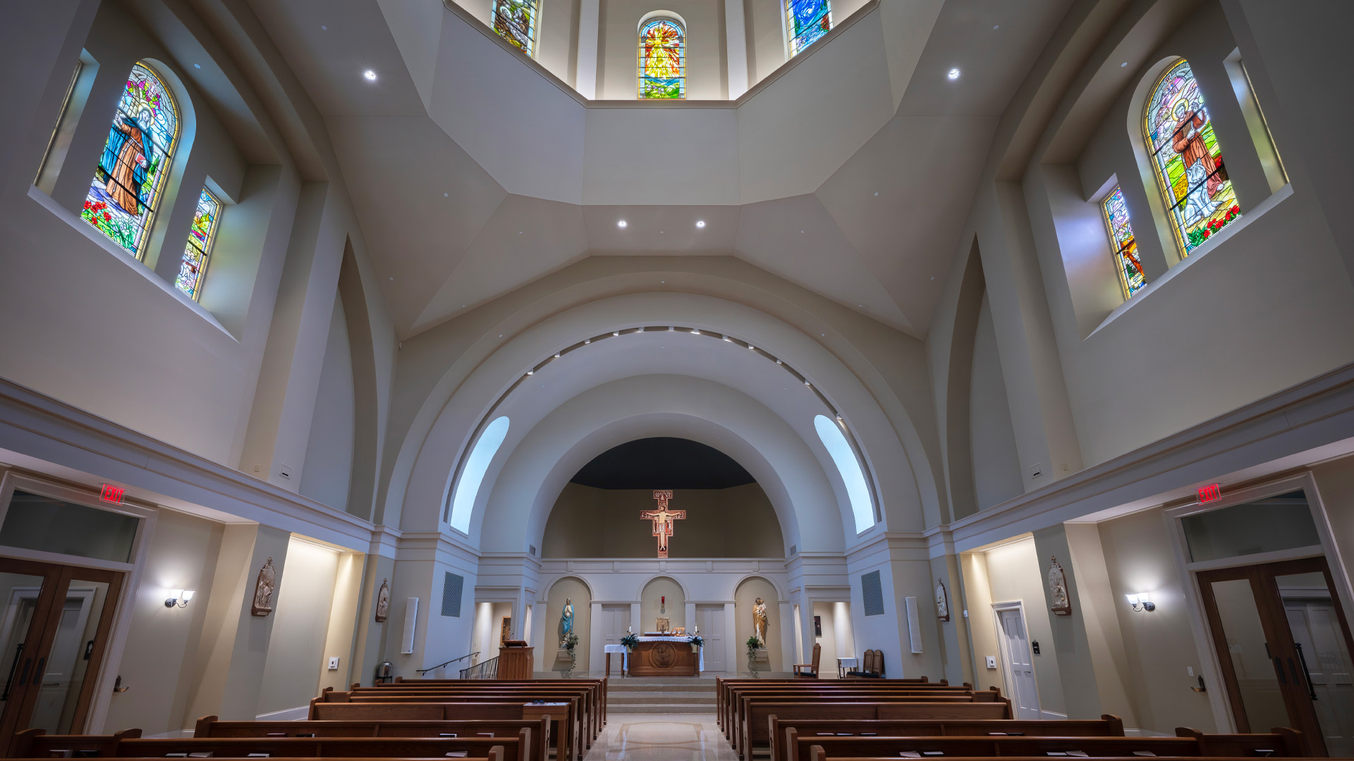 Interior of the University of Saint Francis Chapel of St Francis of Assisi with stained glass windows and a detailed altar with a cross.