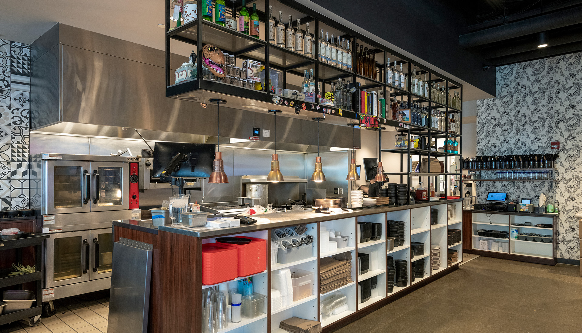A section of the kitchen is visible to guests, allowing them to be part of the creative cooking and dining experience. Sleek equipment, decorative shelving, and deliberate lighting design blend the kitchen and dining spaces.