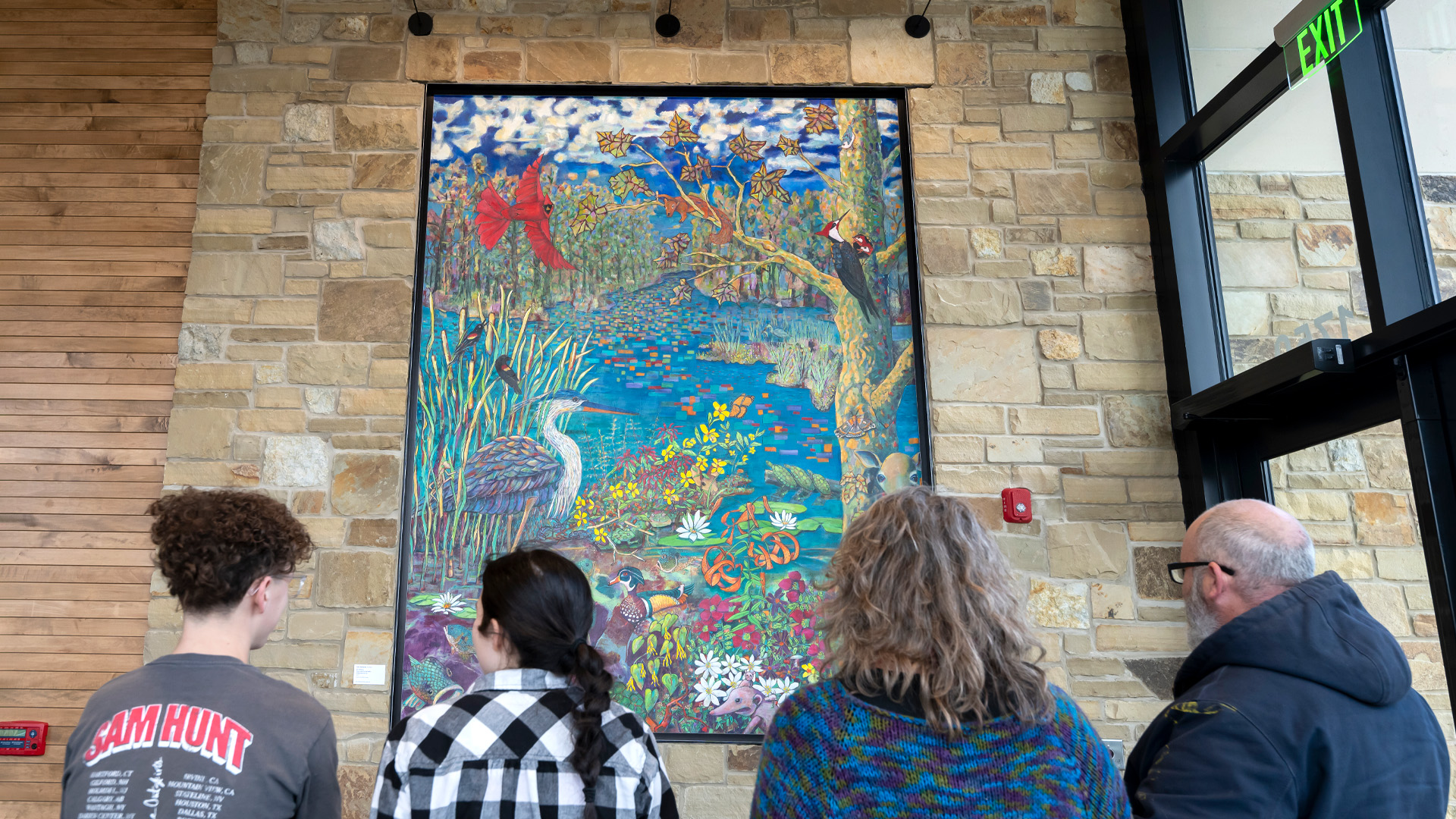 People looking at colorful artwork with animals on stone wall.