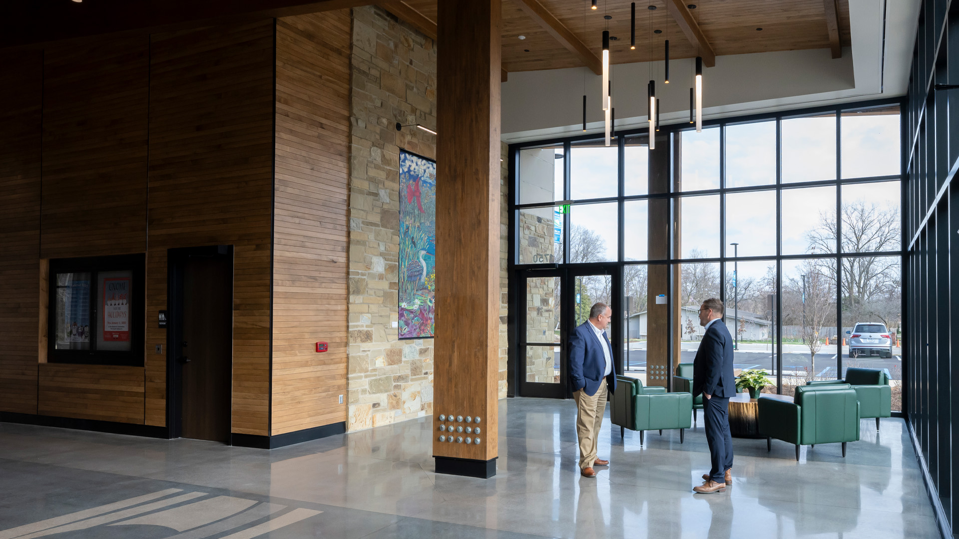 Two men talking in a event center lobby with warm wood tones, large glass windows, and colorful artwork.