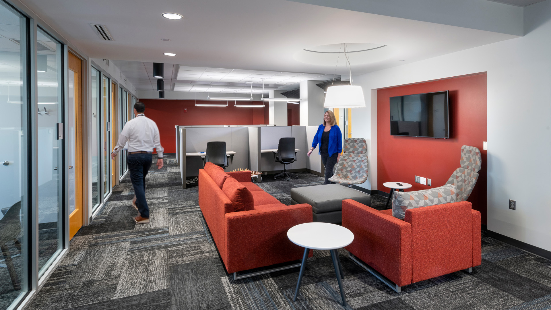 Collaborative student space with private office pods. Space incorporates bold red couches, walls, and gray carpet.