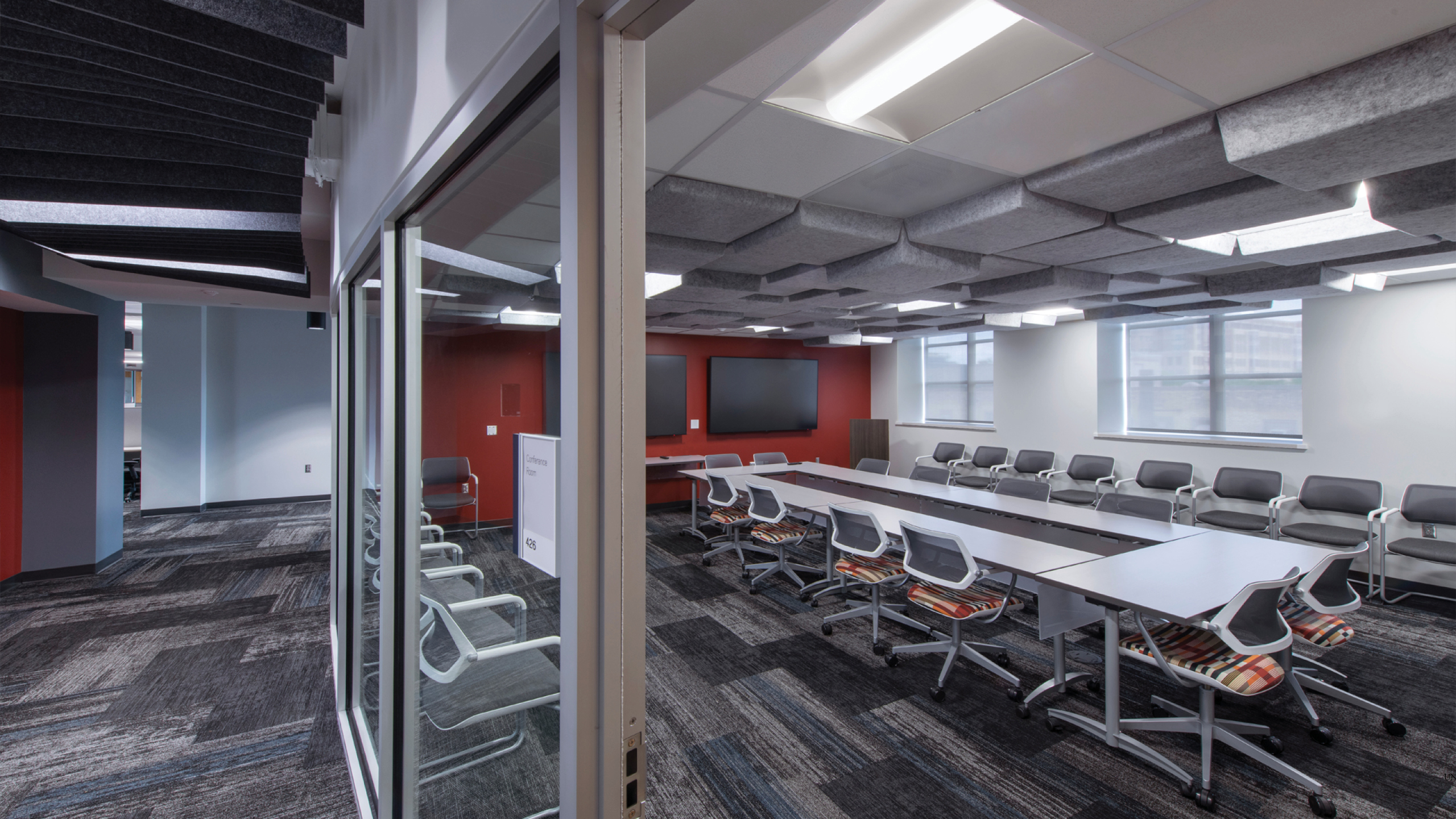 Conference room with red wall, gray carpet, and glass walls for high visibility.