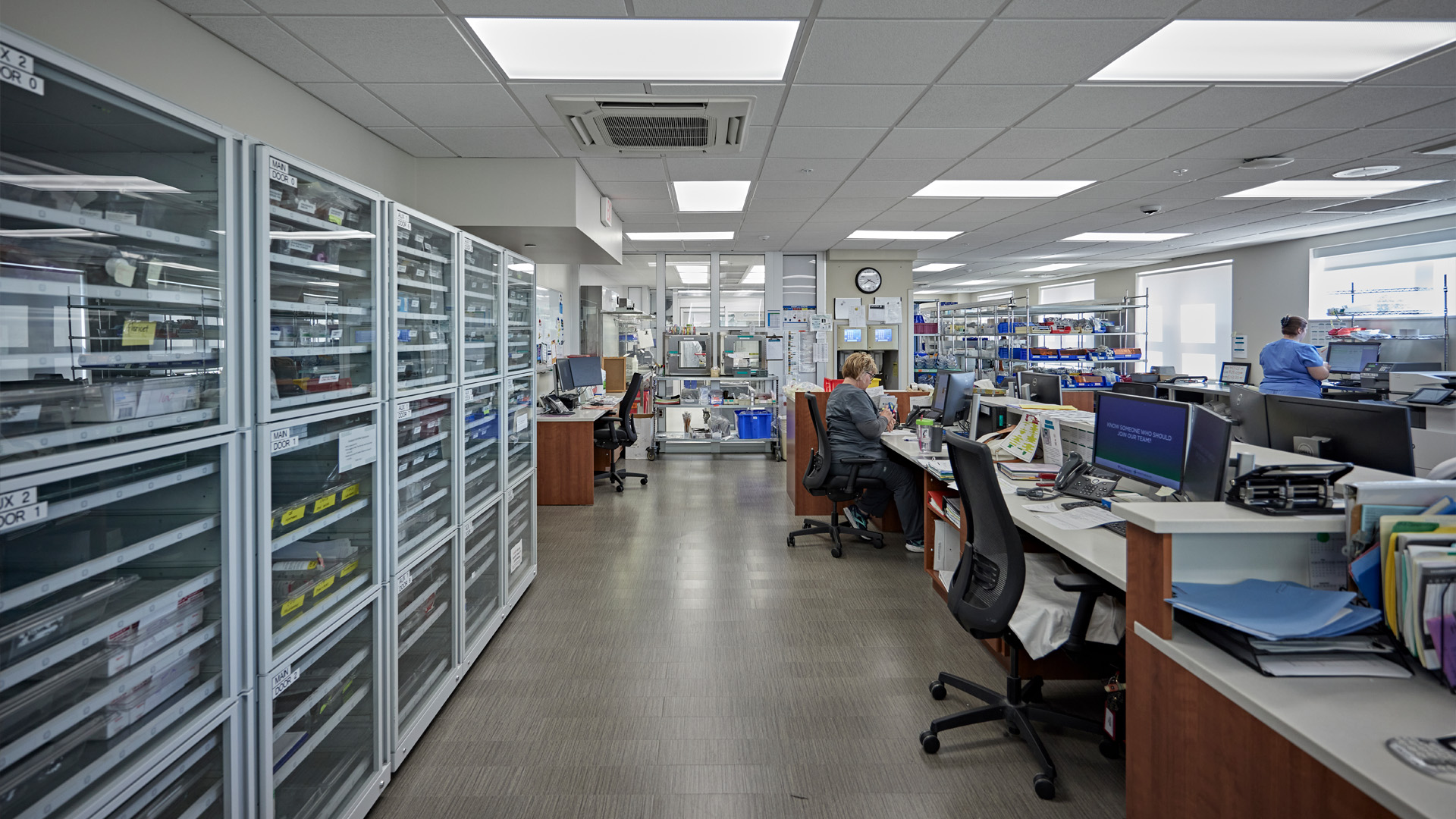 Pharmacy storage room with work spaces and employee working.