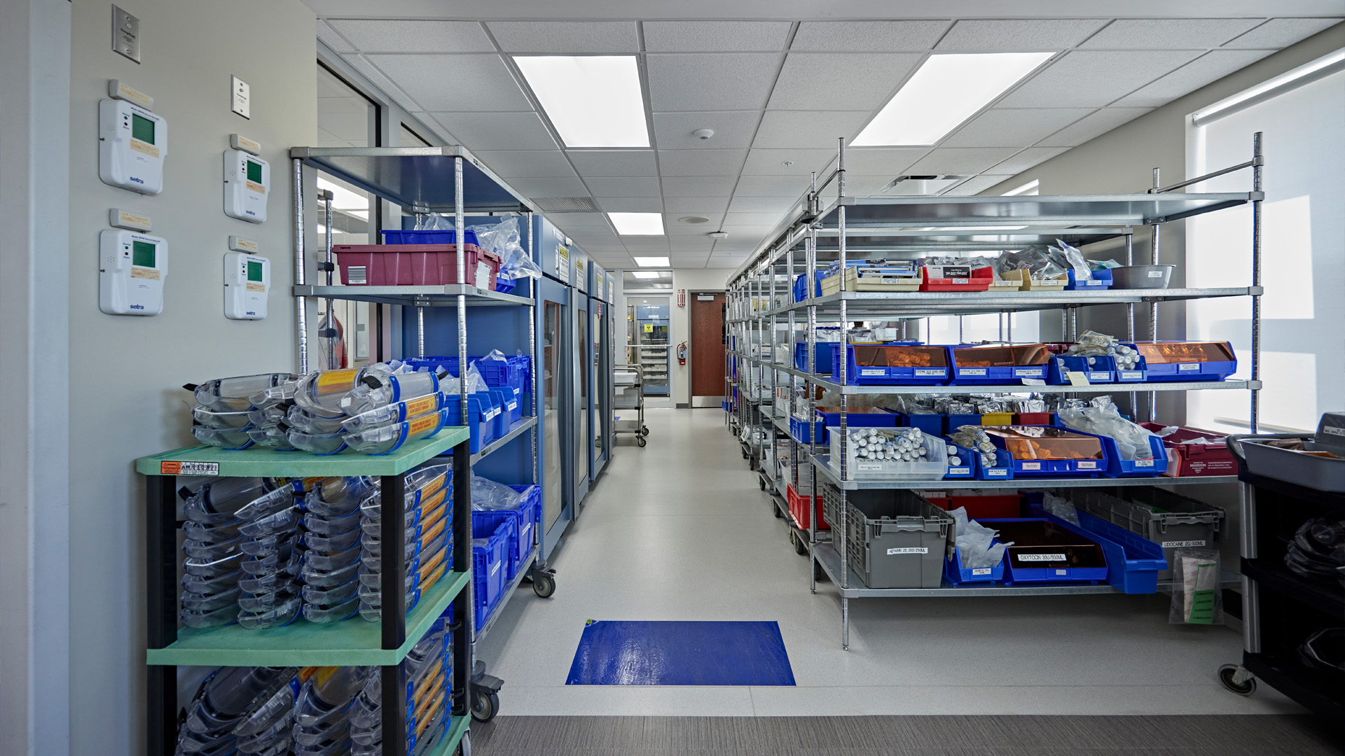 Pharmacy storage room with racks and blue containers.