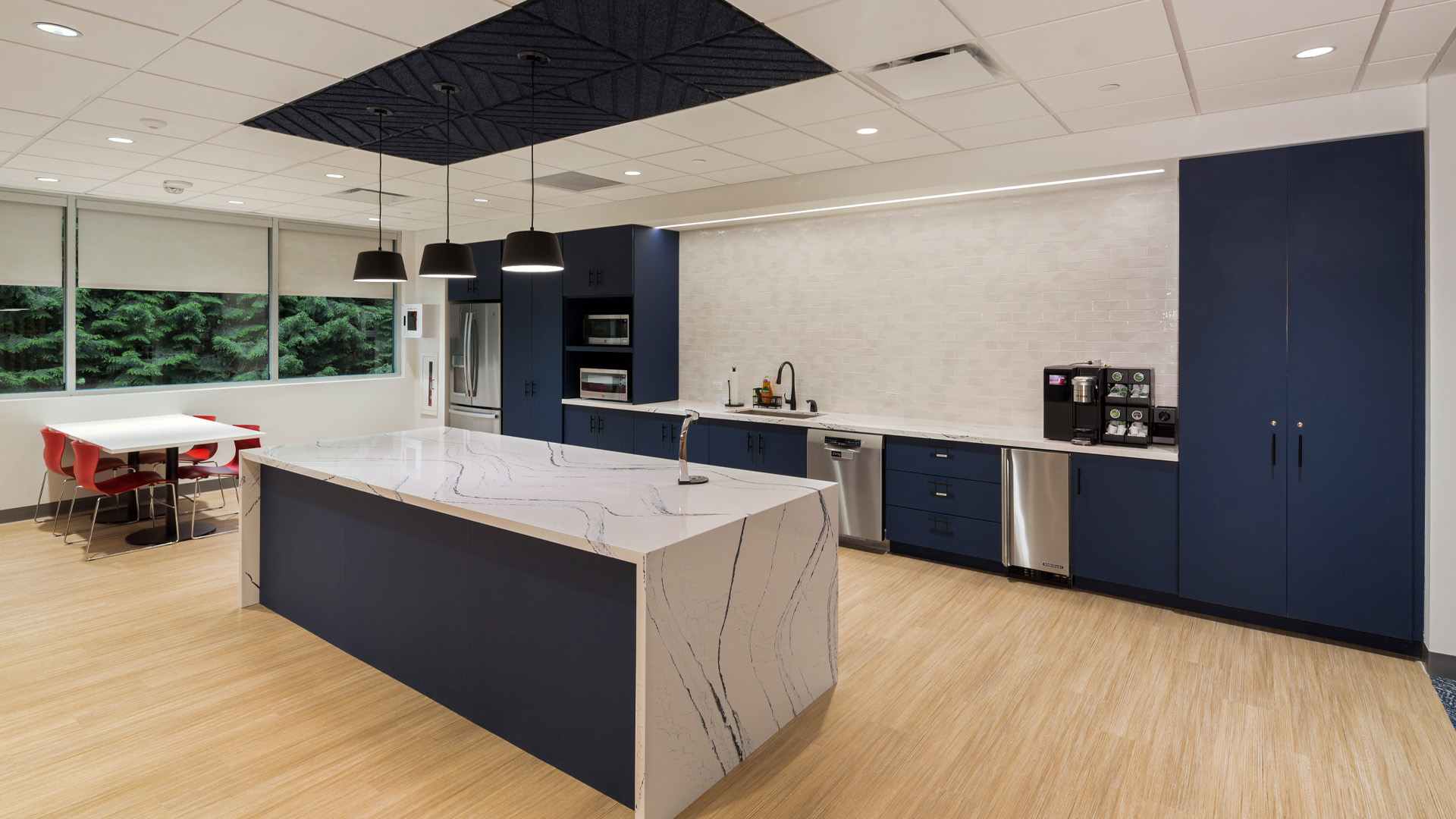 Community hub kitchen with waterfall marble countertops, navy accents, and warm wood flooring.