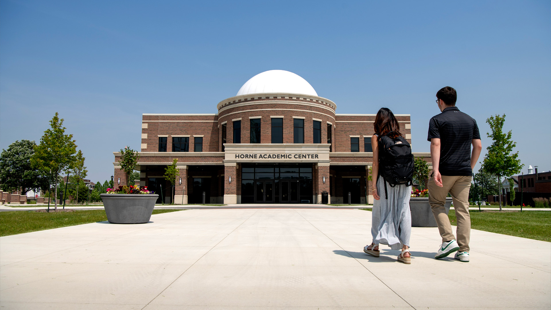 Two students walking into Taylor Univeristy's Horne Academic Center. A brick building with a white dome.