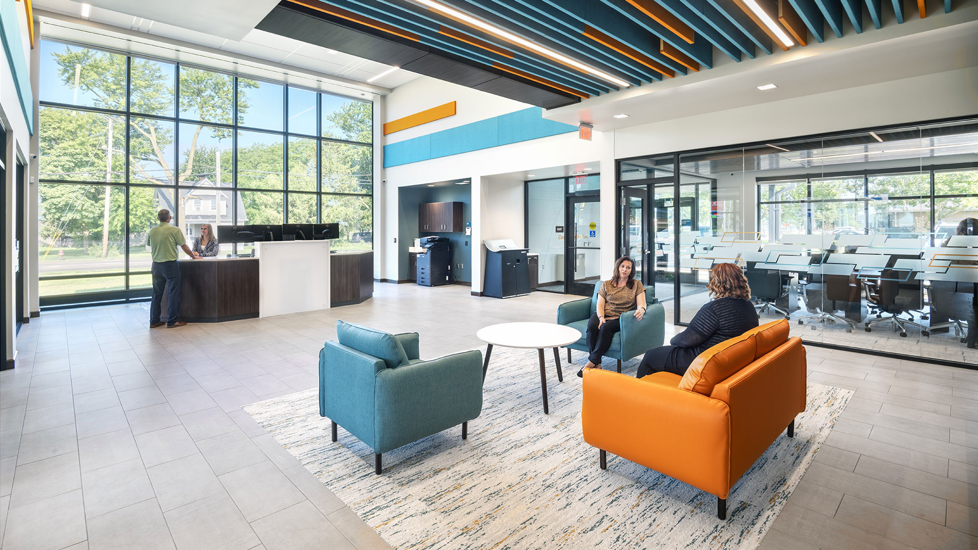 Teller line in bank branch with bright orange and blue branding and large windows.