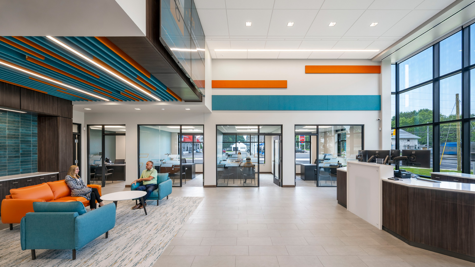 Bank branch lobby with bright orange and blue branding, video wall, and lighting design.