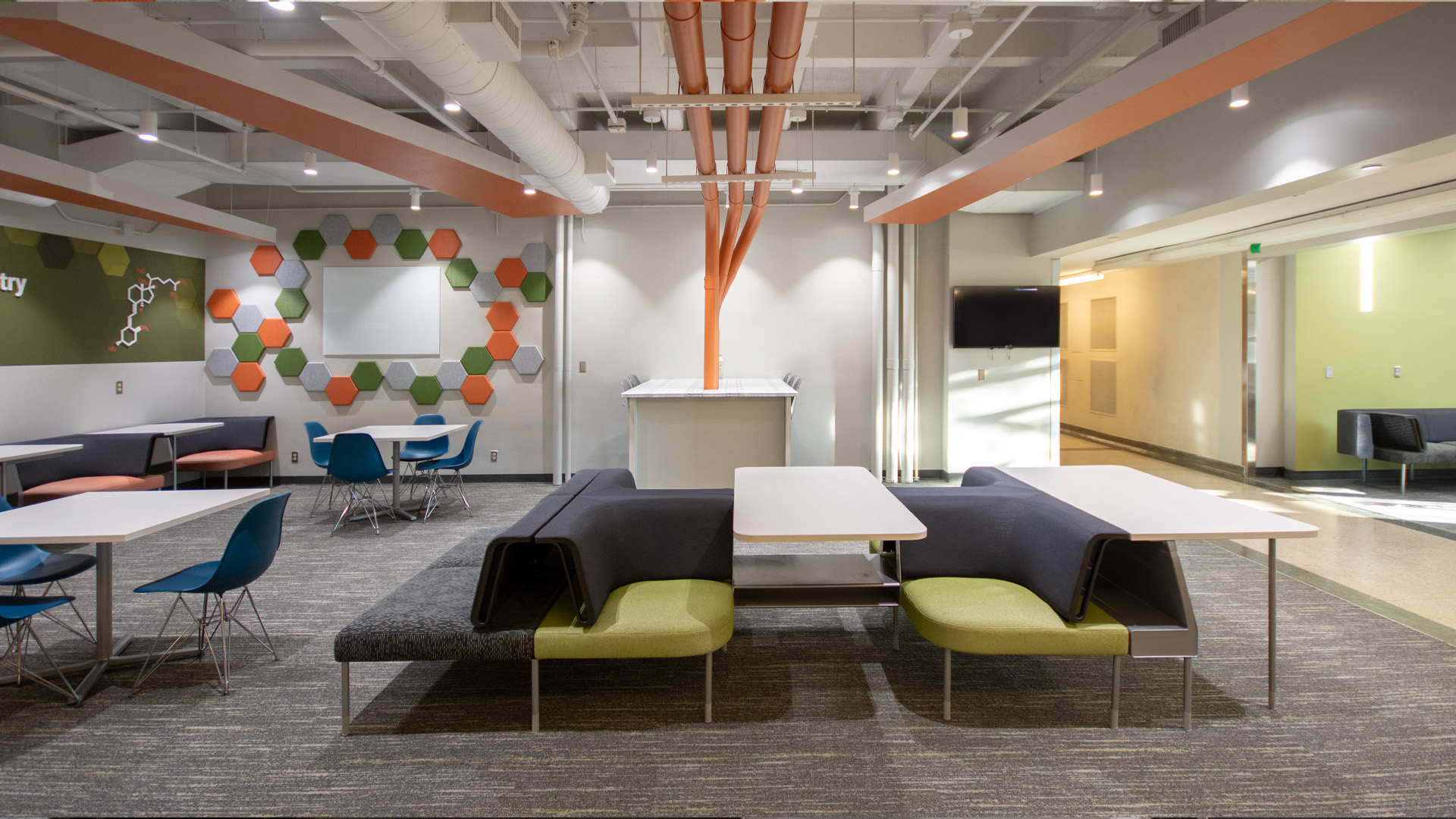 Bold orange, green, and gray textured hex wall audio clouds and various types of seating including booth and chairs and tables.