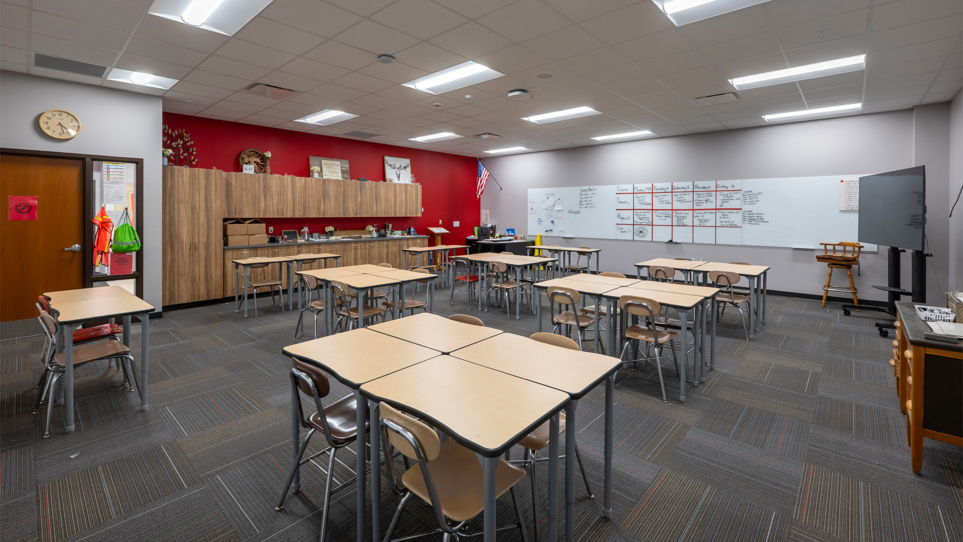 A classroom at Adams Central 400 Wing Addition features tables for collaboration and a red accent wall.
