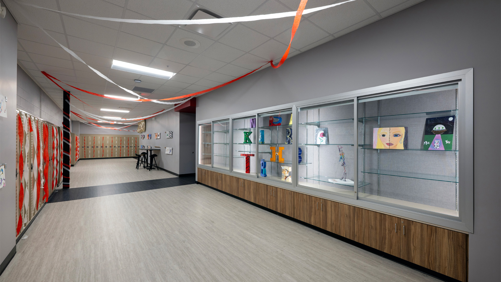 A hallway at Adams Central 400 Wing Addition with beige lockers and a glass display case for artwork.