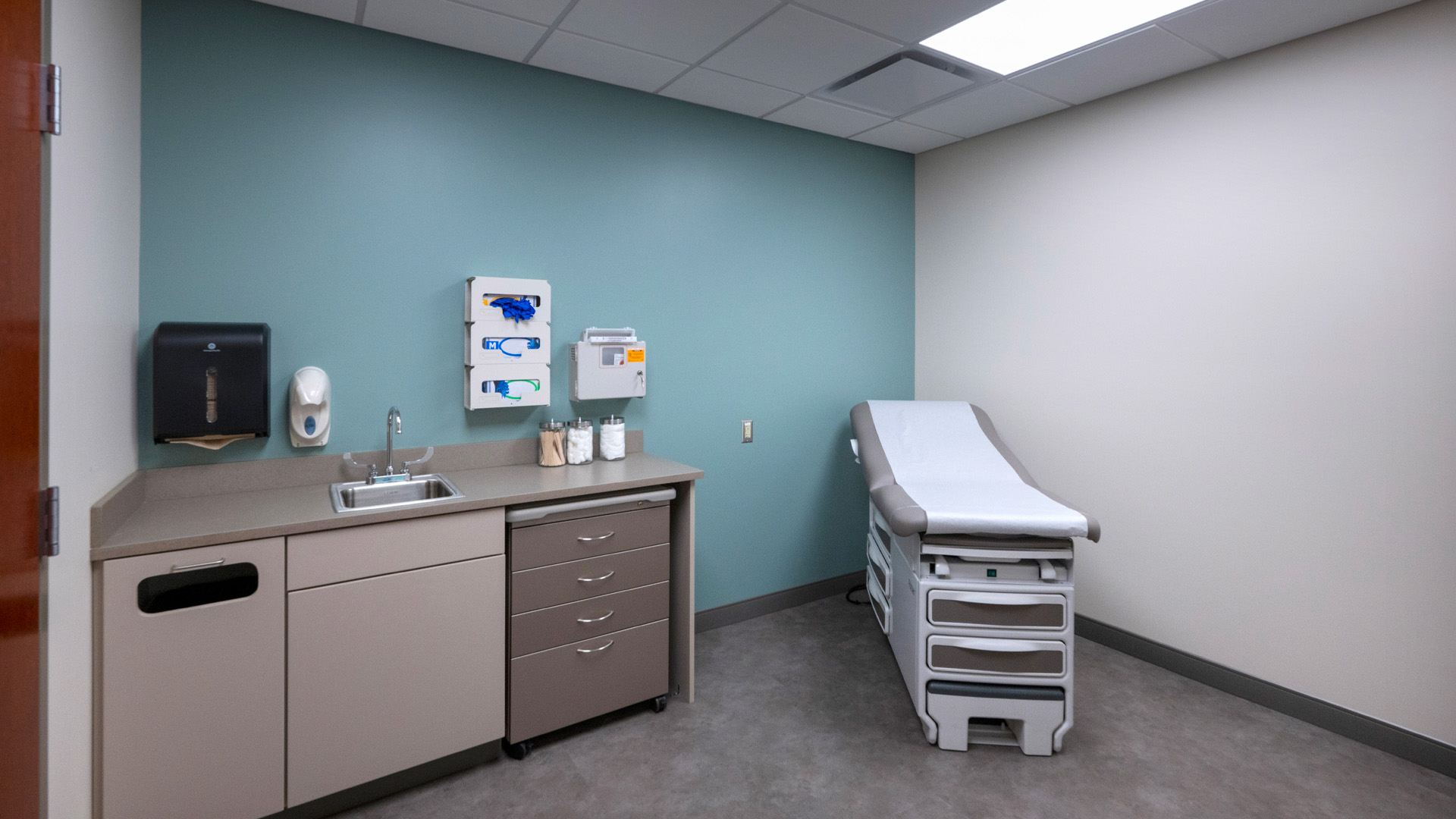 Patient room with teal walls, beige cabinets, and a bed at Parkview Physicians Group Scott Road Clinic.