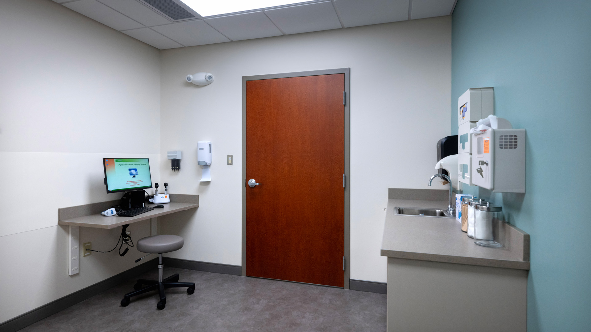 Patient room with teal walls, beige cabinets, and wood door at Parkview Physicians Group Scott Road Clinic.