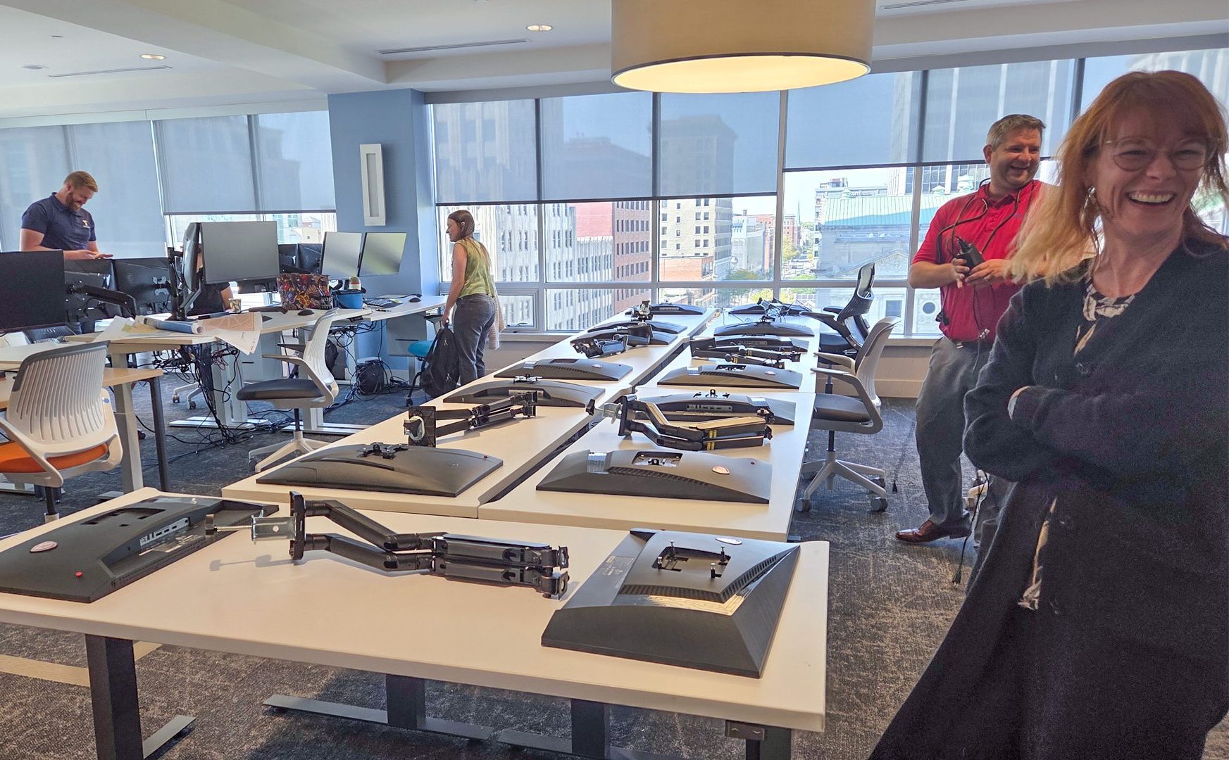 Design Collaborative employees smile at technology being set up in a temporary work space.
