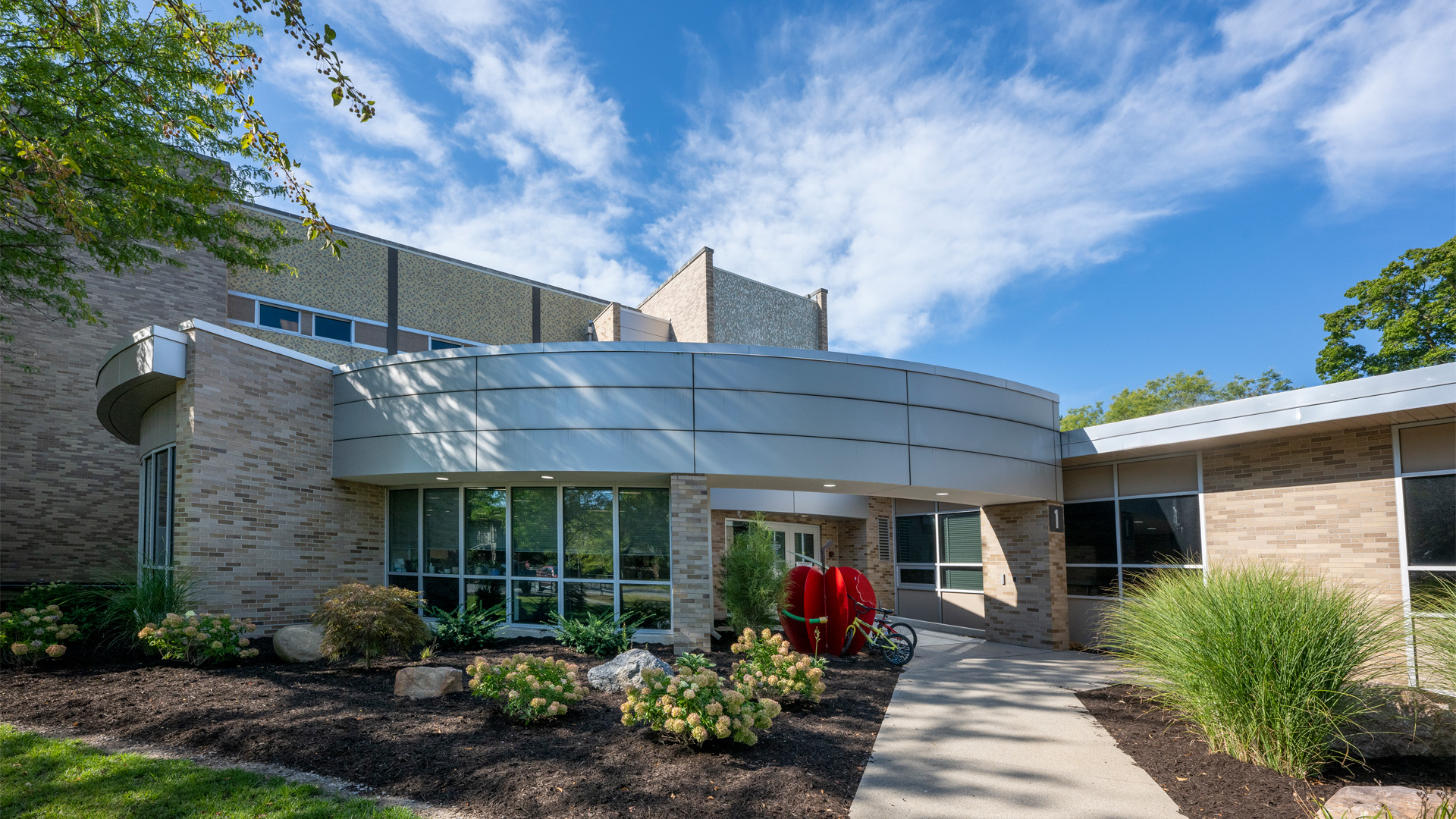 Exterior entrance of the Fort Wayne Community Schools Washington Elementary building with bushes and a decorative apple sculpture.