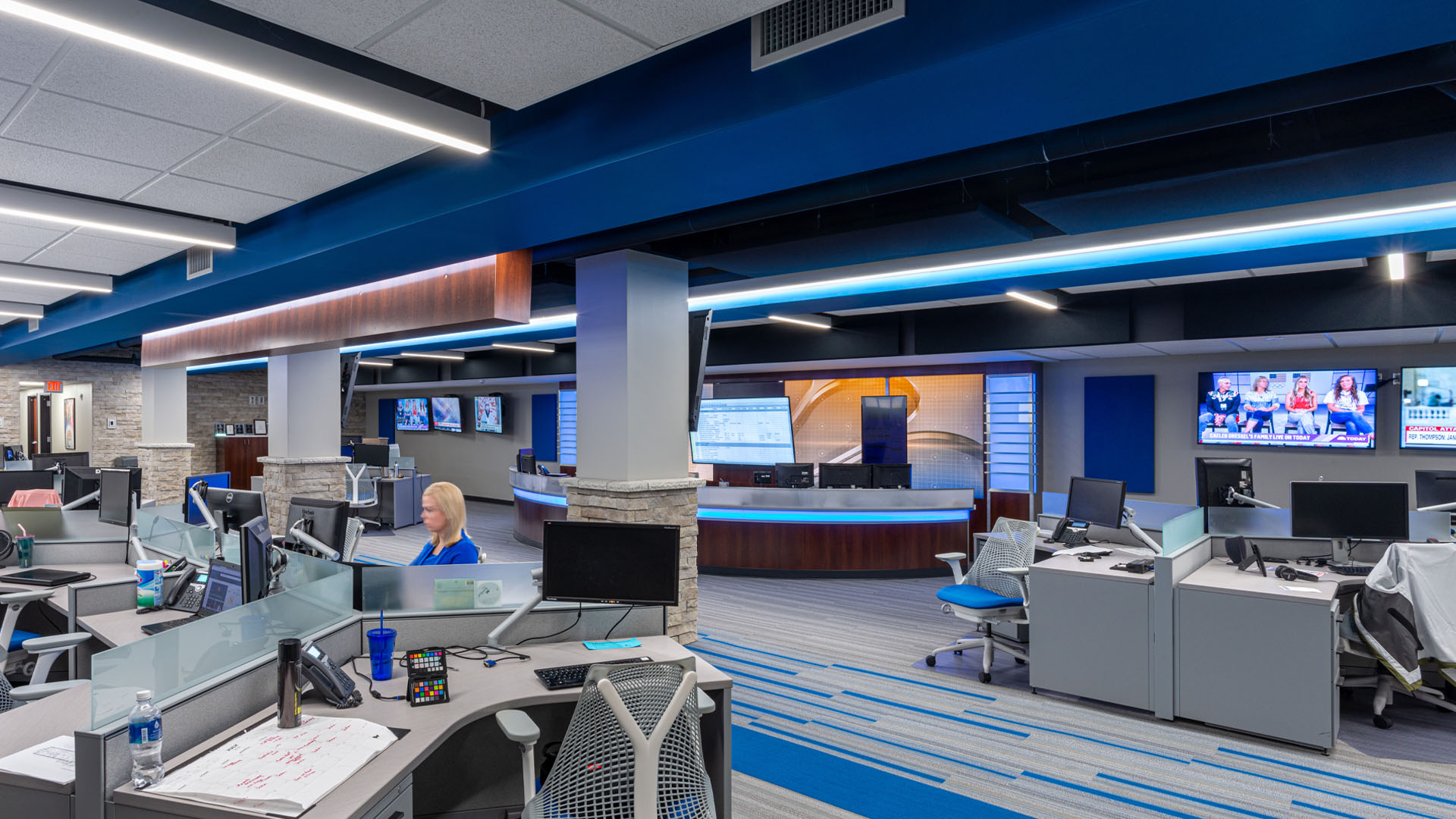 A woman works in the Quincy Broadcasting WGEM news studio with blue accents and an open office layout.