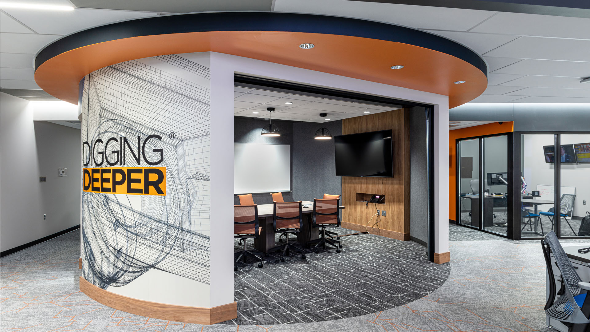 Quincy Broadcasting WSIL-TV Newsroom with colorful orange ceiling details, a graphic wall with a mission statement, and an open office layout. An open circular conference room promotes collaboration in the office.
