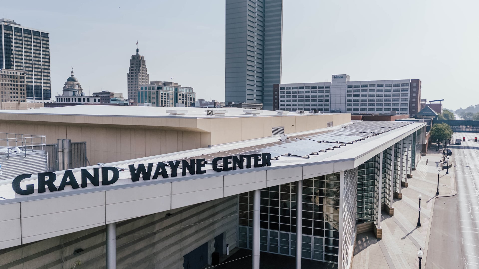 Aerial view of the Grand Wayne Center's new roof upgrades and solar power system with the skyline of Fort Wayne Indiana in the background.
